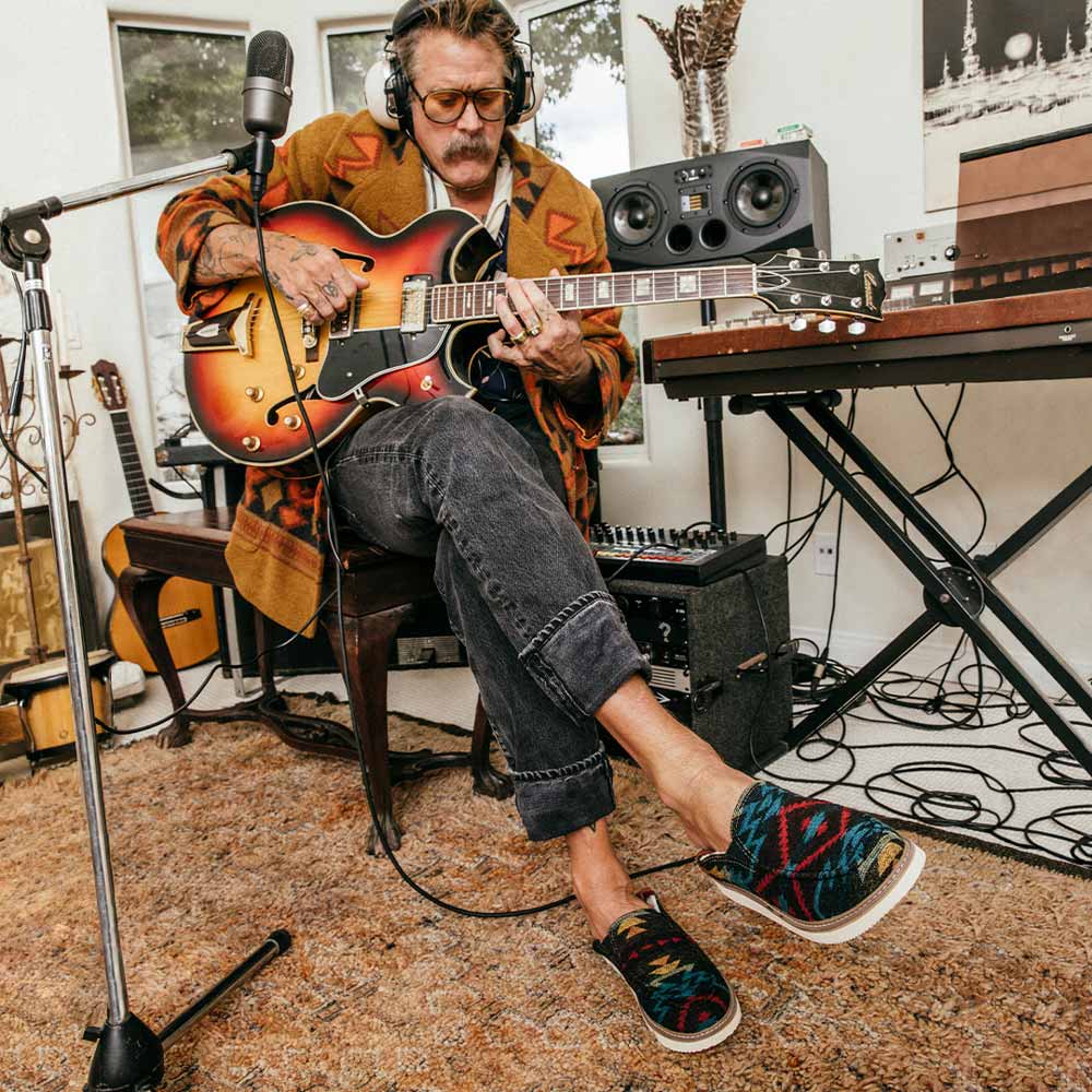 An image of Donavon Frankenreiter, playing a guitar, wearing Sanuk 'Cozy Vibes' shoes.